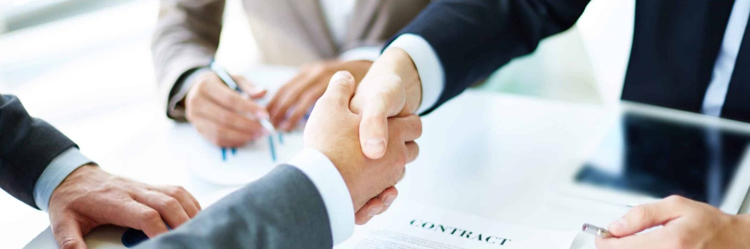 Image of business partners handshaking over business objects on workplace